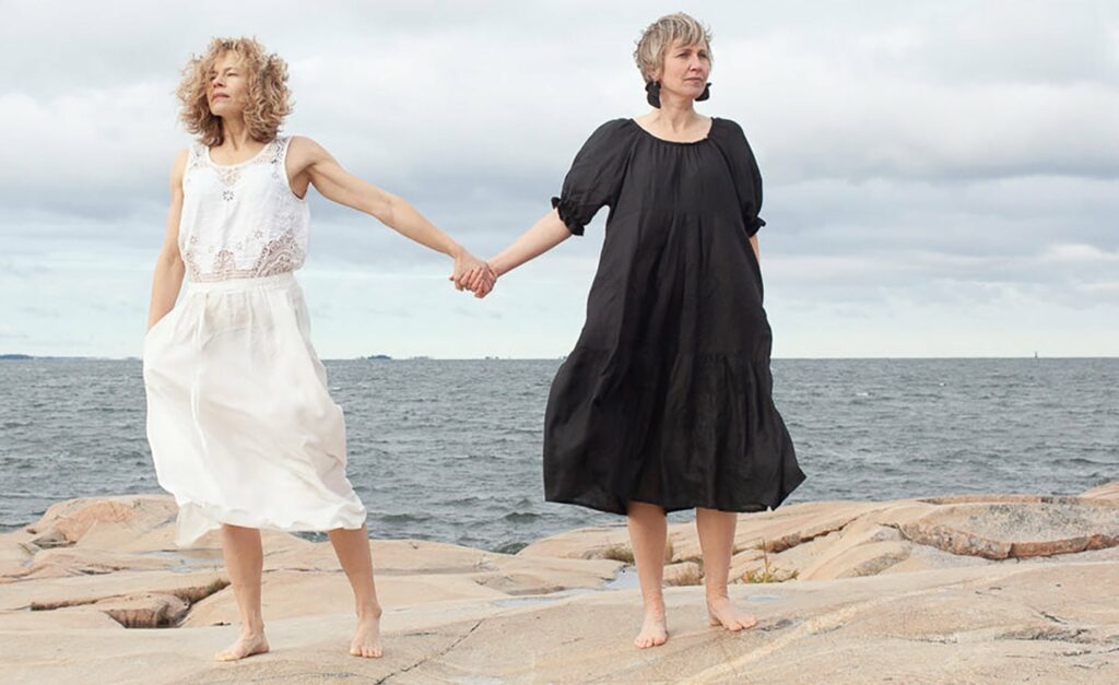 Two women holding hands with the ocean as a background
