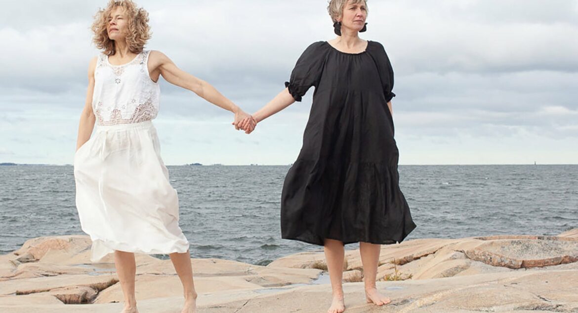 Two women holding hands with the ocean as a background